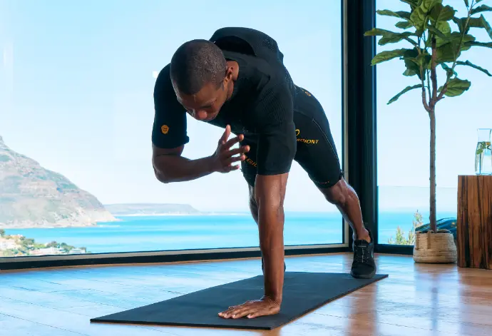 A man in an EMS suit performs a plank exercise indoors, using EMS training to strengthen his arms and build muscle effectively.